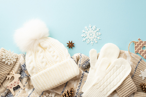 Winter holidays concept. Top view photo of white mittens bobble hat knitted jumper snowflakes pine cones anise and wooden ornaments on isolated pastel blue background