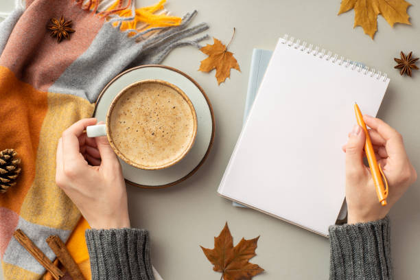 istock First person top view photo of woman's hands in pullover writing in diary holding cup of coffee on saucer scarf maple leaves pine cone and cinnamon sticks on isolated grey background with copyspace 1429428099