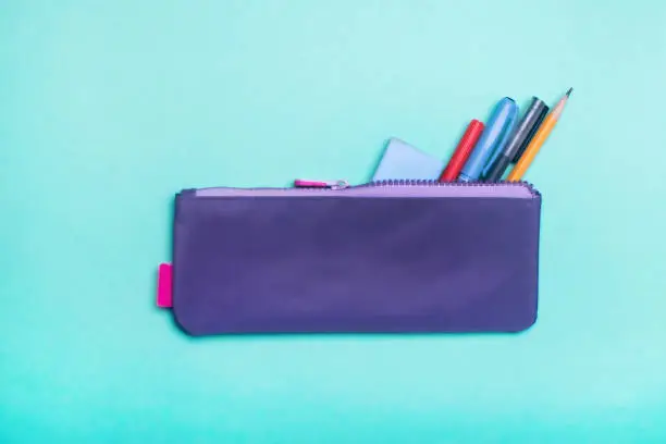 Fashionable violet pencil case with multicolored felt-tip pens, pencils and pens on green background. Back to school.