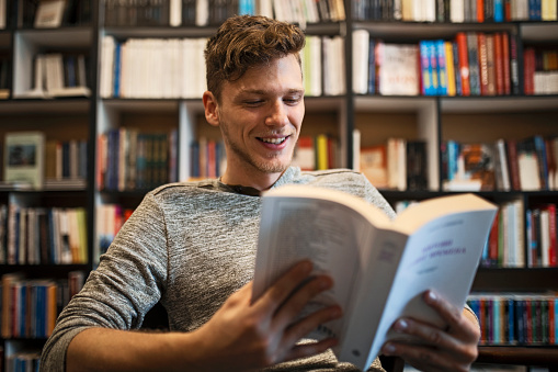 Student in library reading book from bookshelf