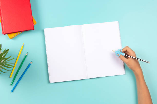 istock Kid hand using pencil with silicone three finger pen. Top view to hand holding pencil with handwriting correction tool and open blank notebook. School, learning difficulties, writing, education 1429434565
