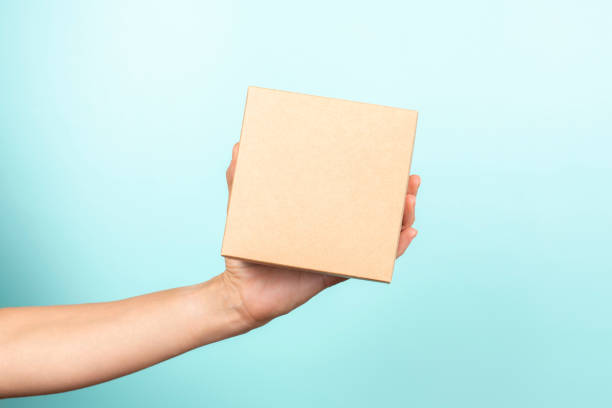 istock Woman hand show small brown rectangular cardboard box on light blue background. Mockup parcel box. Packaging, shopping, delivery, present, gift concept 1429434746
