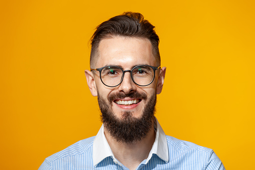 Close up studio portrait of a white 30 year old bearded man with glasses on a yellow background