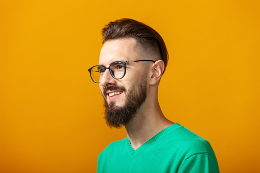 Close up studio portrait of a white 30 year old bearded man in a green sweater with glasses on a yellow background