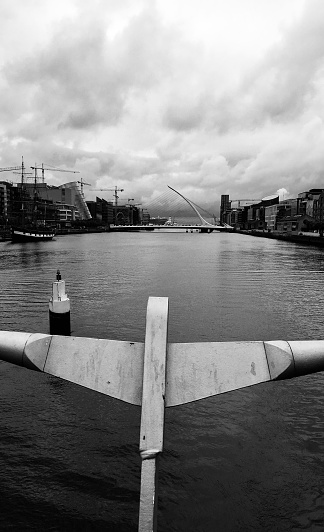 Contrast of old & modern, River Liffey, bridges, quayside buildings, tall ship, cloudy overcast sky.