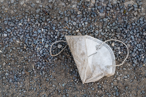Closeup of litter from a lost used disposable face mask fallen on street gravel sidewalk. Eco pollution by covid-19 pandemic.  Waste disposal
