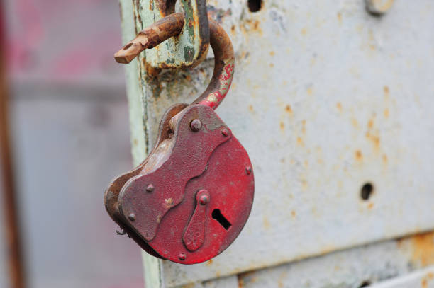 an old red metal open lock hangs on the handle of an iron grey door - antique old fashioned close up color image imagens e fotografias de stock