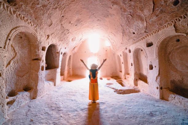 旅行者の若い女の子は、ネブシェヒルのカッパドキア、トルコのカッパドキアでゼルヴェ古代都市の洞窟教会の中で彼女の腕を開いています - ロックフードゥー ストックフォトと画像
