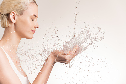 Photo of  young woman with clean skin and splash of water. Blonde woman with drops of water near her face. Spa treatment. Girl washing hands with water. Water and body. Water falling on human hands