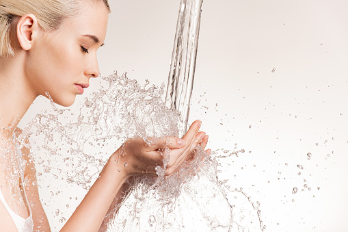 Photo of  young woman with clean skin and splash of water. Blonde woman with drops of water near her face. Spa treatment. Girl washing hands with water. Water and body. Water falling on human hands
