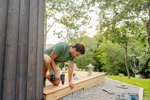 Photo of a carpenter attaching decking boards to a deck of a house.