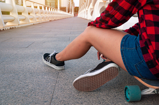 Detail photo of a hipster girl sitting on a skateboard. Sport concept, urban