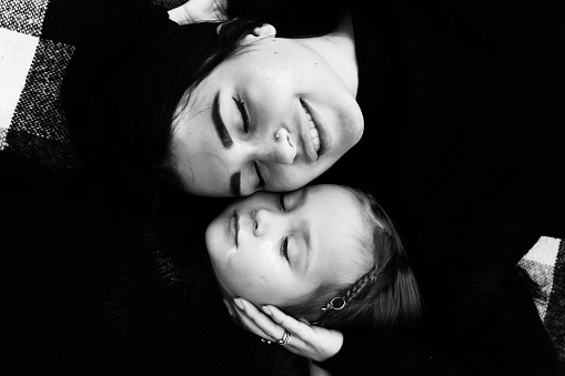 Mom and daughter hugging lie on a plaid. The faces of the woman and the girl are close. Parental tenderness. Black and white photography.