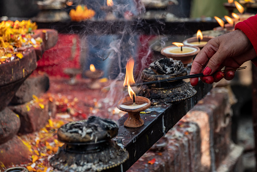 Narayanthan, Kathmandu, Nepal - nov 6, 2019: devout hands of pilgrims light oil candles on the altar where the Vishnu lingam is located in the Budhanilkantha temple in Kathmandu