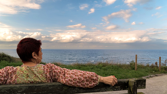 Woman sitting on a bench looking at the horizon. By the sea.
