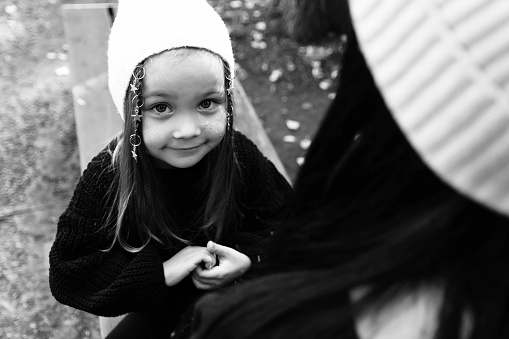 The little girl looks at her mother. Hair ornament. Tenderness. Summer park. Green trees. The concept of a young family. Black and white photography.