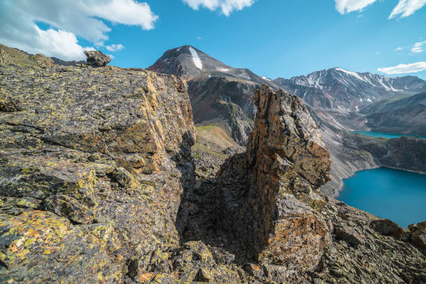 Scenic landscape with sunlit stone outliers with view to two mountain lakes and snow mountains in bright sun. Colorful scenery with sharp rocks and alpine lakes under clouds in blue sky at sunny day. paisaje escénico con valores atípicos de piedra iluminados por el sol con vistas a dos lagos de montaña y montañas nevadas bajo un sol brillante. paisaje colorido con rocas afiladas y lagos alpinos bajo las nubes en el cielo azul en un día soleado.