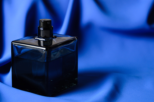 A bottle of black glass with a perfume spray on a wavy blue background. Selective focus.