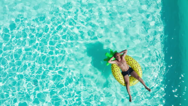 4K drone footage zooming in on man floating on water in swimming pool sunbathing.