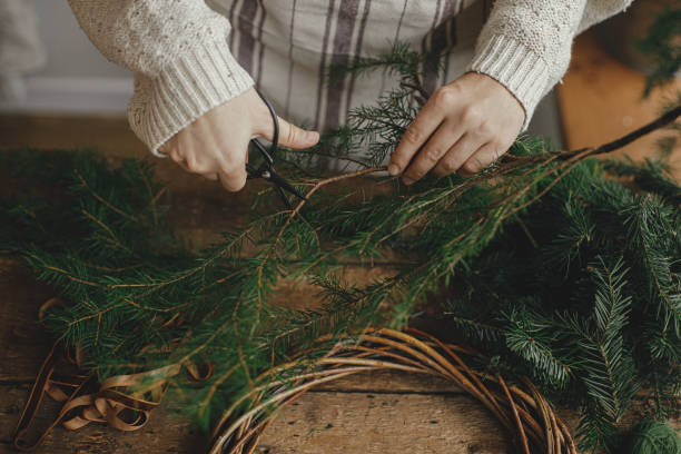 istock Making rustic Christmas wreath. Female hands cutting fir branches with scissors on background of rustic wooden table with ribbon. Moody Christmas image, holiday preparations 1429532360