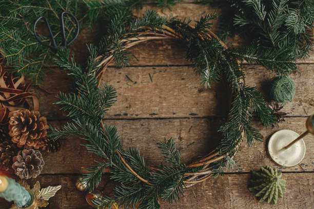istock Making rustic Christmas wreath flat lay. Fir branches on round wicker wreath, pine cones, ribbon, golden bells and candles on rustic wooden table. Moody Christmas still life, holiday preparations 1429532585