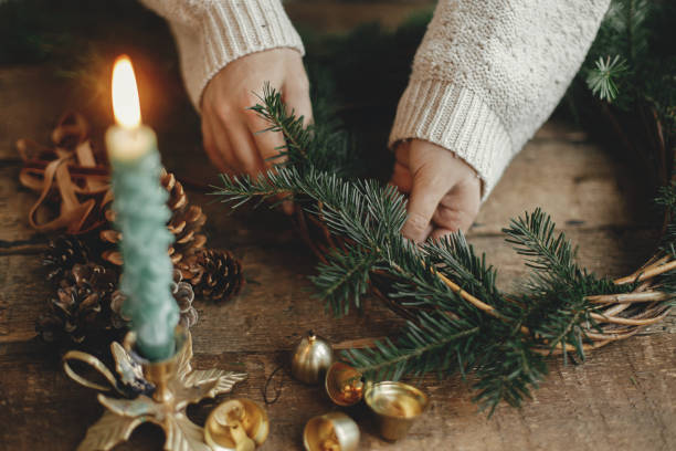 istock Making Christmas rustic wreath. Woman hands holding fir branches and making wreath on rustic wooden table with ribbon, golden bells, candles. Moody holiday image. Winter holiday workshop 1429533783