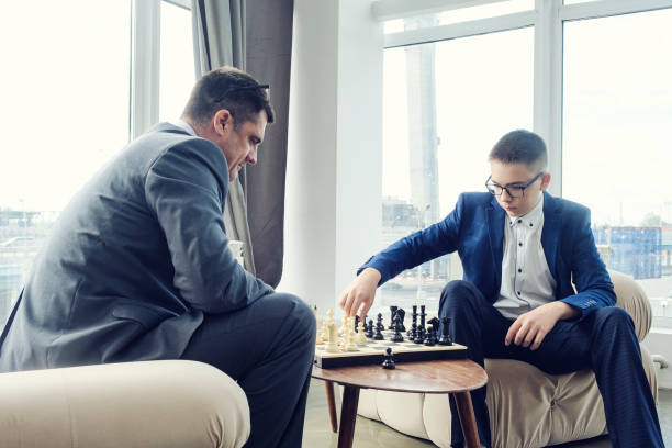 istock dad and son are sitting at a table by a wide window and playing chess making moves with pieces 1429547856