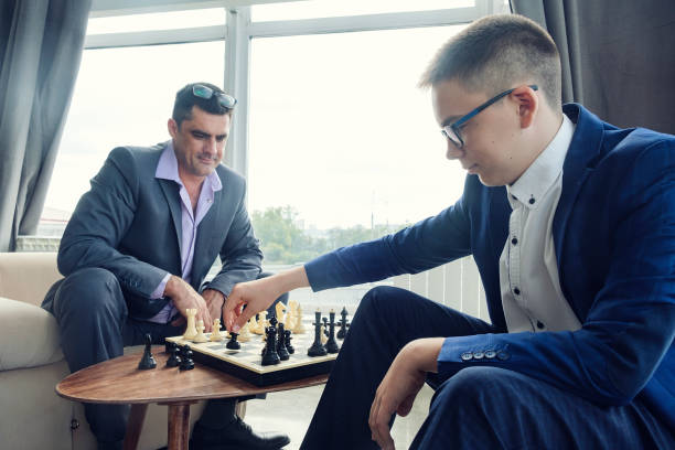 istock dad and son are sitting at a table by a wide window and playing chess making moves with pieces 1429547857