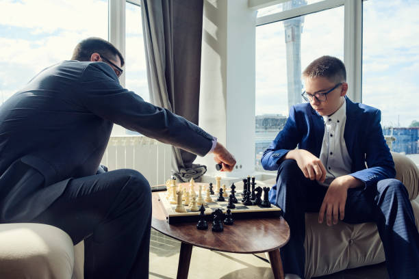 istock dad and son are sitting at a table by a wide window and playing chess making moves with pieces 1429547894
