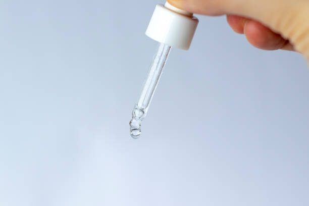istock Small cosmetic pipette with a transparent serum in hand, dripping on the table 1429548484