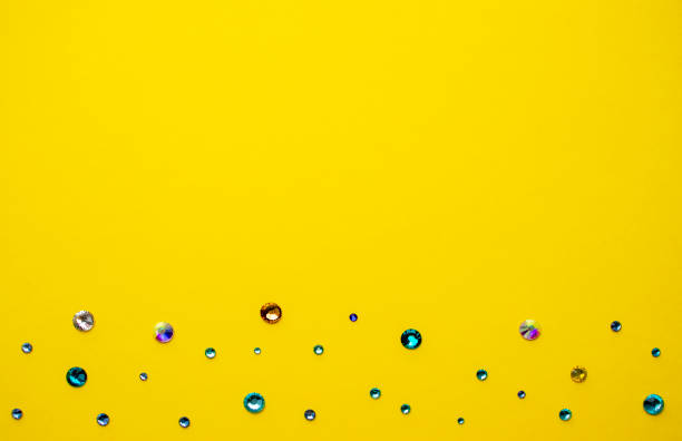 istock Multicolored rhinestones on yellow background, top photo. Design for text. 1429549974