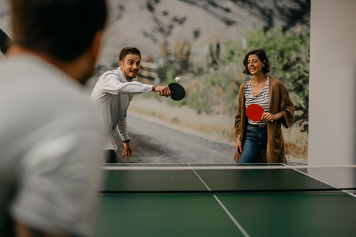 Colleagues are playing table tennis at work and having some fun at the office. Image of a business people in casual clothes playing ping pong.