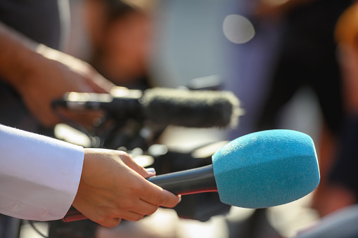 Group of people, female politician confronted by journalists with microphones.