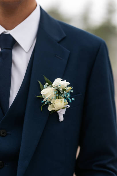 Boutonniere on the groom's blue jacket Close-up of the groom's wedding boutonniere of cream eustoma or rose flower and green leaves pinned to a blue jacket against a background of a white shirt and tie. Wedding accessory. buttonhole flower stock pictures, royalty-free photos & images