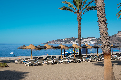 Umbrellas and sun loungers on the beach of Almuñecar bathed by the water of the Mediterranean Sea, Spain