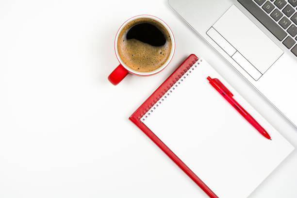 Red coffee cup with red notepad and pen, laptop keyboard on white background
