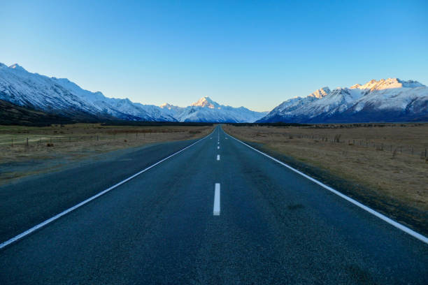 Mountain Road Journey Mount Cook Road looking towards Aoraki Mount Cook in the Southern Alps.  This image was taken at sunset in early Spring. middle of the road stock pictures, royalty-free photos & images