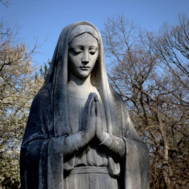 istock Statue of Virgin Mary praying against bare trees 1429592324