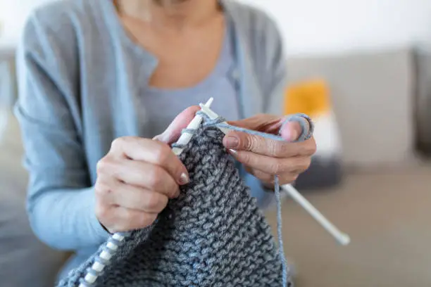 Grandmother holding needles make repetitive motion knitting sitting on couch creating something with her arms. Hand knitting improve brain function, older generation hobby concept