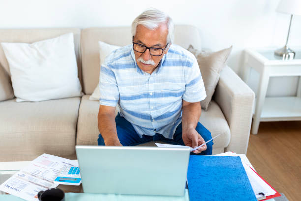 istock Focused grey-haired elderly man sit on couch reading bank notifications calculating domestic expenditures, concentrated modern mature male consider financial paperwork, pay bills on laptop online 1429596648
