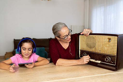 Small child listening music from a tablet while his grandmother from an old radio