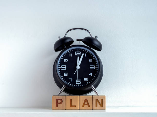 istock Planning concept. Words PLAN on wooden cube blocks and black vintage alarm clock with after midnight time on clock face isolated on white background. 1429599866