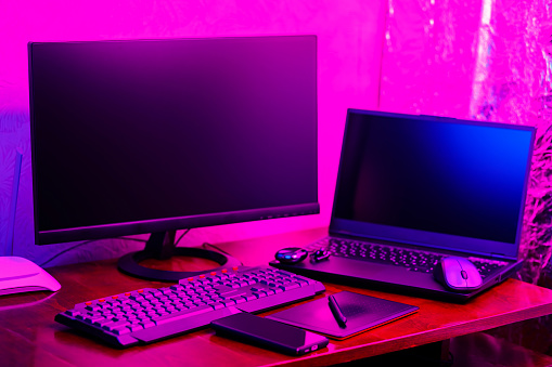 Workplace of a graphic designer and creative retoucher. Graphic tablet, smartphone and computer equipment in neon light. Workspace of creative designer with tablet and stylus