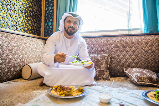 Middle eastern man wearing kandora eating in a cafè restarant in Dubai