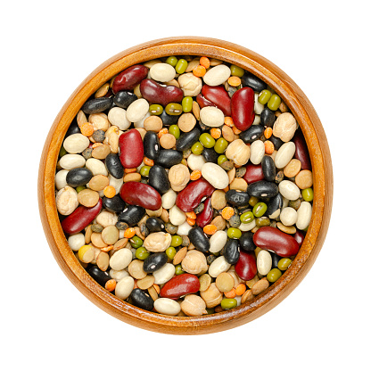 Mixed dried pulses in a wooden bowl, from above. Colorful mix of red kidney, black and white beans, mung beans, brown, green and red lentils, and chickpeas. Isolated, on white background, food photo.