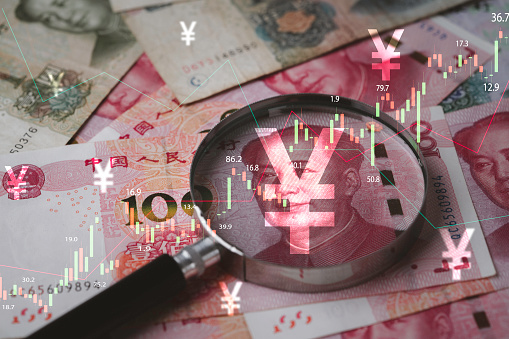 Closeup on magnifier glass with Mao Tse Tung on Yuan banknote and stock market graph for currency exchange and Interest rates concept.