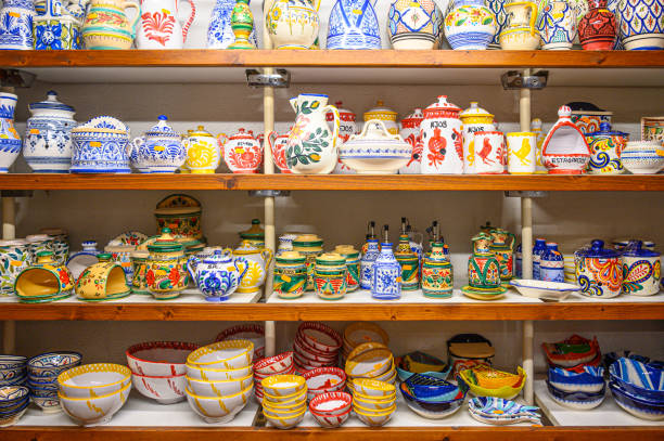 Alicante, Spain - October 4, 2022: A collection of ceramic bowls, jugs, plates, cups, and other articles displayed on a store's wooden shelves. There are no people on the scene.