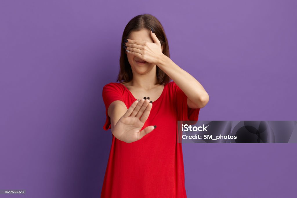 Ugh, how gross is that. Frowning young pretty brunette girl in red t-shirt covering eyes with hands and doing stop gesture with disgusting. Posing over purple background. Ugh, how gross is that. Frowning young pretty brunette girl in red t-shirt covering eyes with hands and doing stop gesture with disgusting. Posing over purple background 20-24 Years Stock Photo