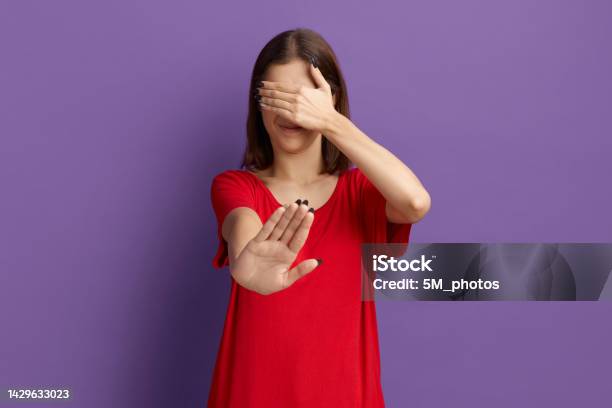 Ugh How Gross Is That Frowning Young Pretty Brunette Girl In Red Tshirt Covering Eyes With Hands And Doing Stop Gesture With Disgusting Posing Over Purple Background Stock Photo - Download Image Now