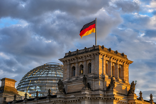 Top of the Reichstag Building with dome and National flag of Germany at sunset in city of Berlin, Germany.
